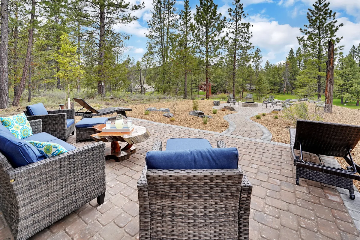 A tranquil outdoor seating area with comfortable chairs overlooks a winding pathway and natural landscaping, inviting guests to unwind with a book or enjoy a meal outdoors. The abundance of trees and clear sky hint at the vast recreational spaces and beautiful scenery available just beyond the property.