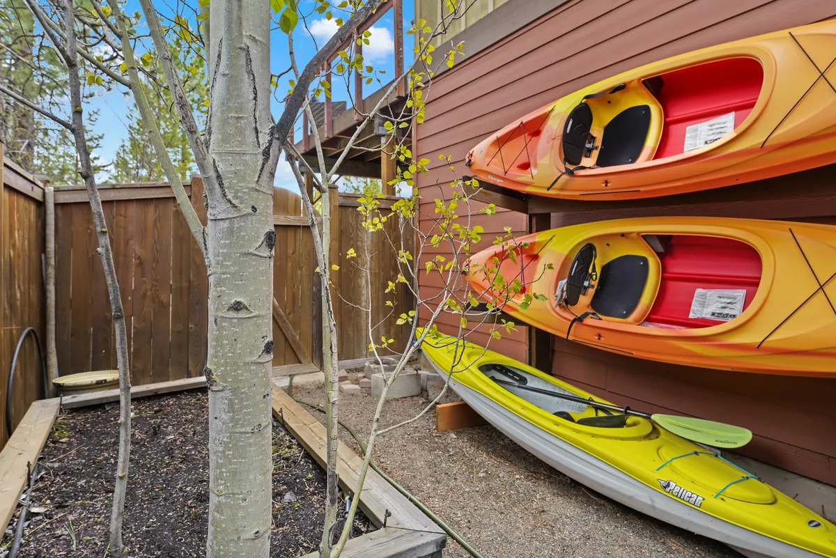 Brightly colored kayaks rest near a wooden fence and aspen tree, suggesting adventure and river access. The scene hints at active outdoor fun and the convenience of launching right from the property.