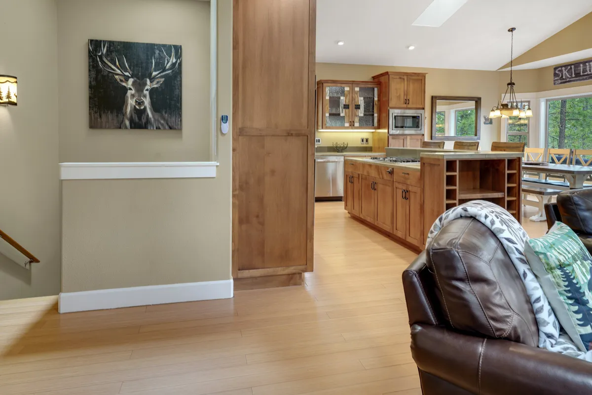 This image captures an open-concept space with a view of the kitchen island, dining area, leather sofa, and a prominent deer portrait on the wall. The flow between kitchen, dining, and living areas supports easy movement and togetherness, echoing the idea of a communal hub.