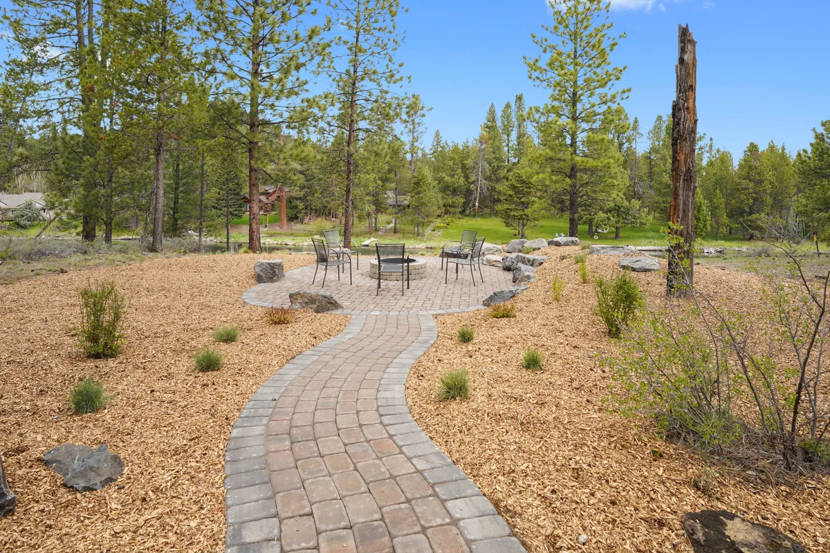 This inviting exterior image highlights a pathway leading to a fire pit and seating area amidst a backdrop of tall trees. The setting suggests both moments of communal gathering and the opportunity for stargazing or recounting the day's adventures around the fire in a tranquil natural landscape.