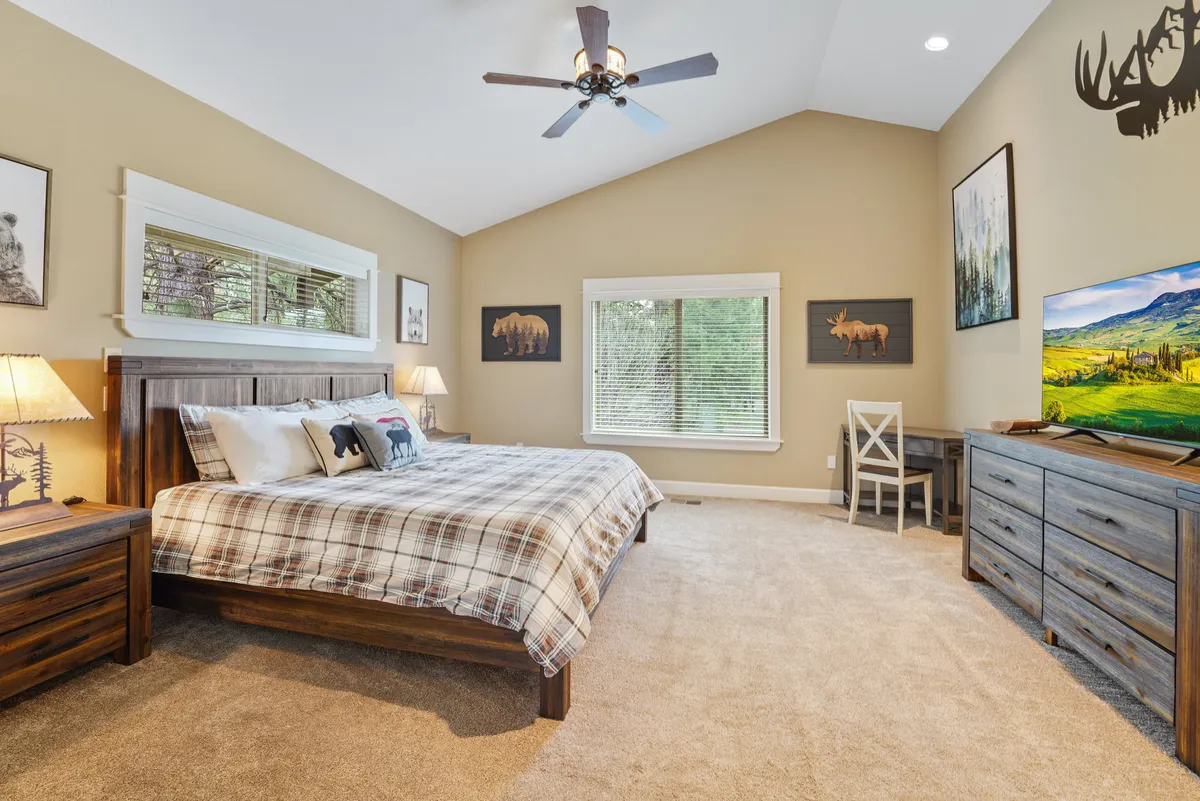 A spacious bedroom with a large bed dressed in plaid bedding, accented by wooden furniture and wall artwork. A generous window bathes the room in natural light, creating a peaceful and inviting atmosphere perfect for relaxation and sleep.