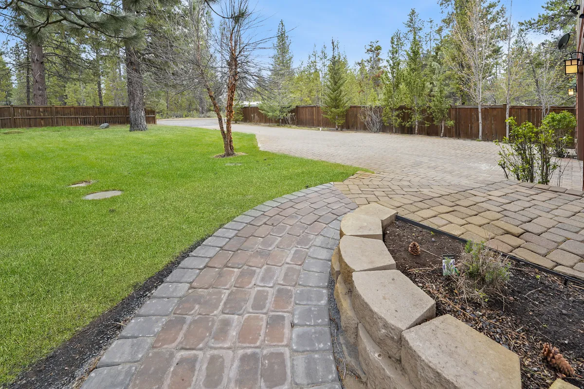 A peaceful winding pathway cuts through a lush green lawn, bordered by mature trees and a low stone wall. The setting is tranquil and inviting, ideal for leisurely strolls with pets or simply enjoying the fresh air. The wide grassy area and surrounding natural beauty create an open, secure space that pets and their owners would enjoy exploring together.