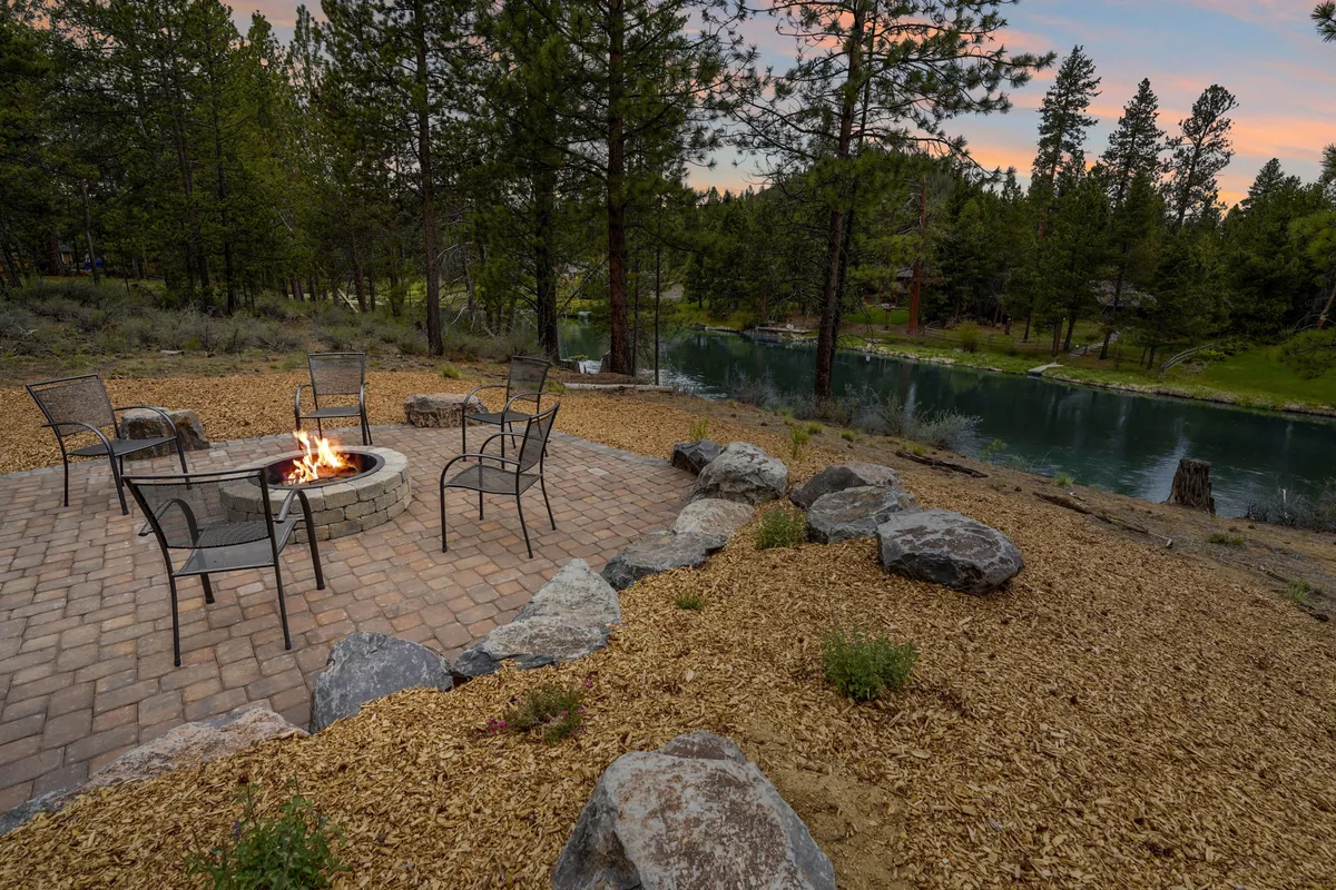 This image features a cozy fire pit surrounded by comfortable chairs, set along the river's edge with trees framing the scene. The tranquil setting invites gatherings for storytelling, marshmallow toasting, and stargazing, with the gentle flow of the river providing a serene backdrop.
