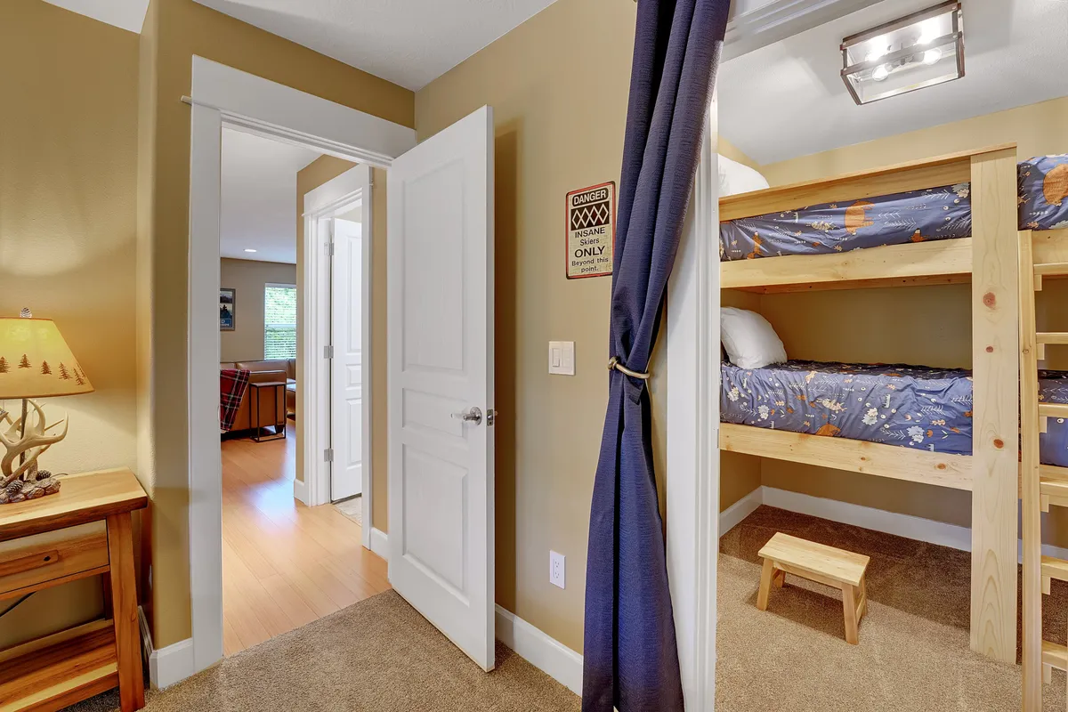 A whimsical nook with a bunk bed, wooden stool, lamp, and playful curtain, creating a snug hideaway ideal for kids or groups. The cozy design encourages imaginative play and comfortable rest.