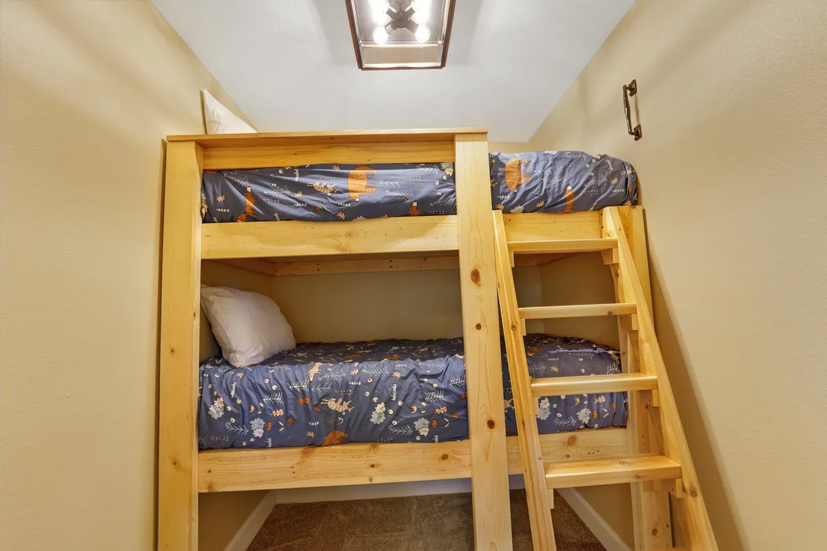 A playful bedroom with sturdy wooden bunk beds, textured bedding, and a ladder, designed for children or group sleepovers. The mood is warm, cheerful, and family-friendly.