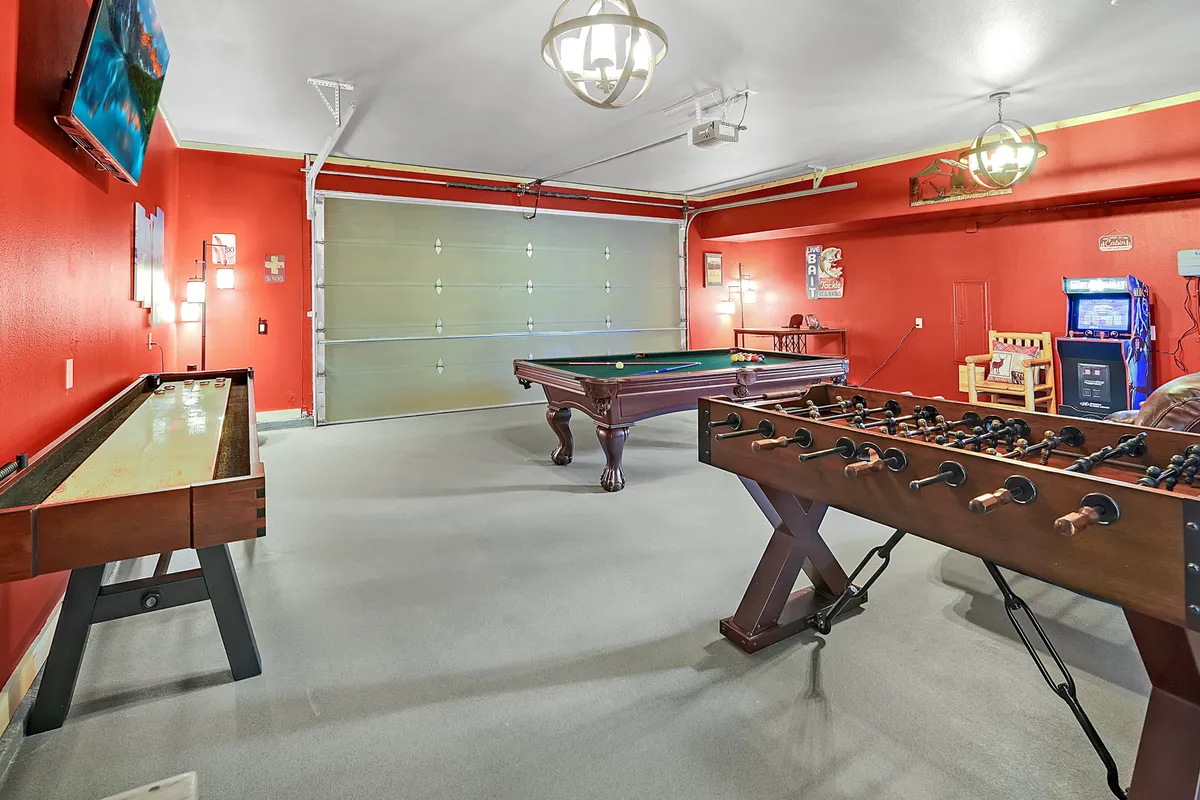 A spacious game room featuring a pool table, foosball table, shuffleboard table, and a classic arcade machine. The space is well-lit and organized, perfect for group play and lively competition.