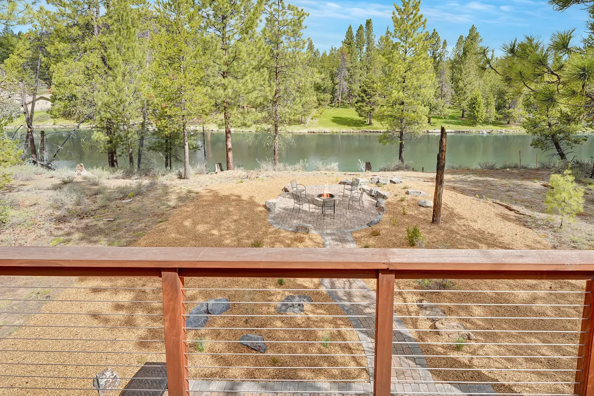 The scene shows a fire pit and seating area beside a peaceful water body, with a meandering pathway and tall trees completing the natural setting. The setup is ideal for relaxing by the fire, enjoying sunset views, and engaging in birdwatching or photography.